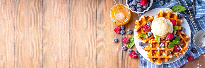Tasty Homemade Belgian waffles with raspberries, blueberries, vanilla ice cream and syrup or honey, sweet summer healthy breakfast, light wooden background copy space 