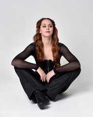 Full length portrait of beautiful woman with long red hair wearing sheer corset top and leather...