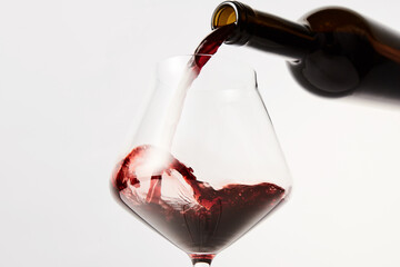 Red wine pouring into tilted wineglass from bottle.