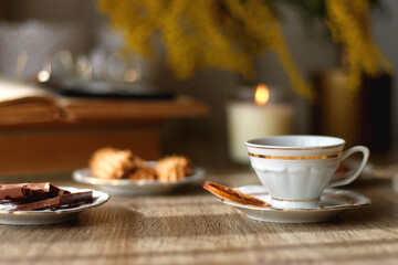 Scented candles, chocolate, cookies, cup of tea, books, e-reader, glasses and flowers on the table. Hygge at home. Selective focus.
