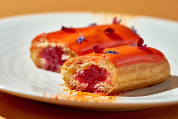 Cut in half eclair with berry filling and custard in a plate. Close-up, shallow depth of field
