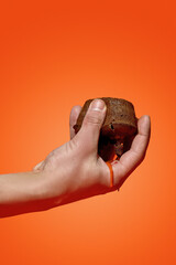 A man's hand holds a chocolate fondant from which chocolate flows on an orange background