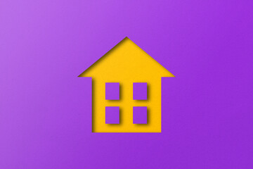 Yellow paper cut out house shape isolated on purple paper background.
