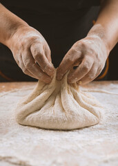 Hands of a woman kneading dough on a wooden table