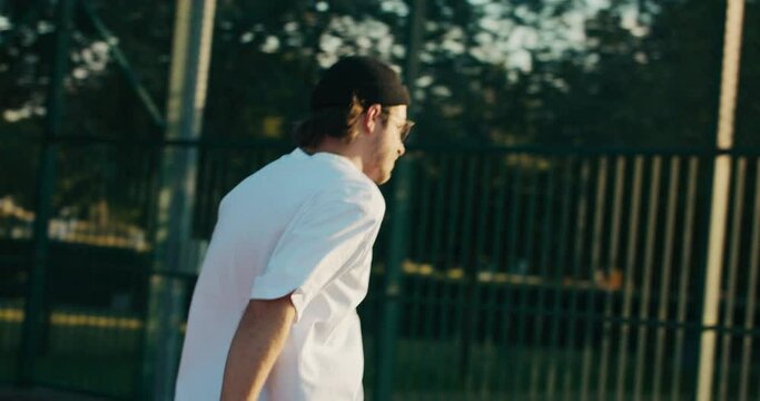 Young fashionable handsome man takeshsmartphone from ground after hard basketball game at playground. Portable audio speaker. Battery powered speaker. - Powered by Adobe