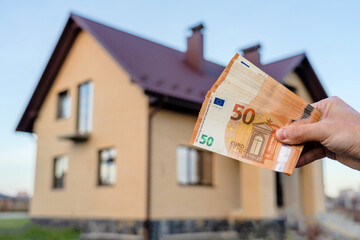 Man's hands hold money standing in front of home. Real estate, leasing insurance, purchase concept