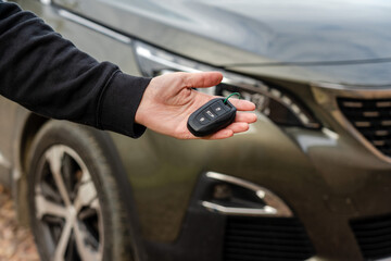 Person holding a car key in the hand stands front car. Insurance, loan and buying car concept