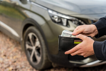 Person holding a wallet in the hands stands front car. Insurance, loan and buying car finance concept