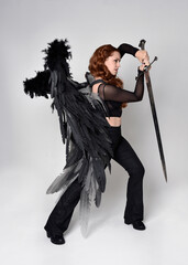 Full length portrait of beautiful woman with red hair wearing corset, leather pants, large black...