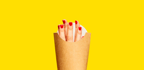 Female fingers instead of fries into packaging against yellow studio background. Surrealism and creativity. Food pop art photography. Imagination. Complementary colors. Copy space for ad, text