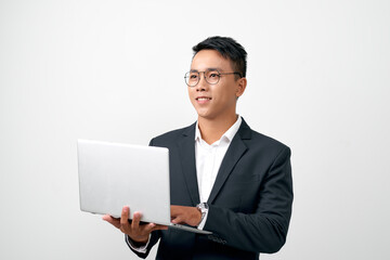 Confident young handsome man in black suit holding open grey laptop and smiling while standing