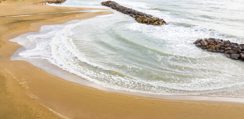 Aerial view of an artificial gulf enclosed by two breakwater in the Mediterranean Sea.  There is no one on the sandy beach.