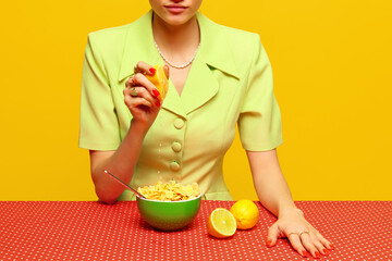 Cropped image of woman in retro suit squeezing lemon juice into cereal against pink studio...