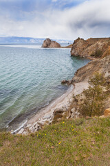 Beautiful spring  landscape of Baikal Lake. View of famous Shamanka Rock or Burkhan Cape and cost of Olkhon Island from green lawn with yellow dandelions. Natural background. Spring travels