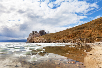 Picturesque spring landscape of Baikal Lake. White ice floes float near the famous Shamanka rock - a natural landmark of Olkhon Island. Nature background. Spring travel and outdoor recreation