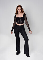 Full length portrait of beautiful woman with long red hair wearing black corset top and leather...