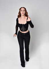 Full length portrait of beautiful woman with long red hair wearing black corset top and leather...