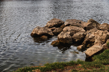 Urban landscape. View of the city pond. An urban landscape with a lake and large rocks near the shore, and a clear sky. Beautiful view of the lake or river with reed grass.