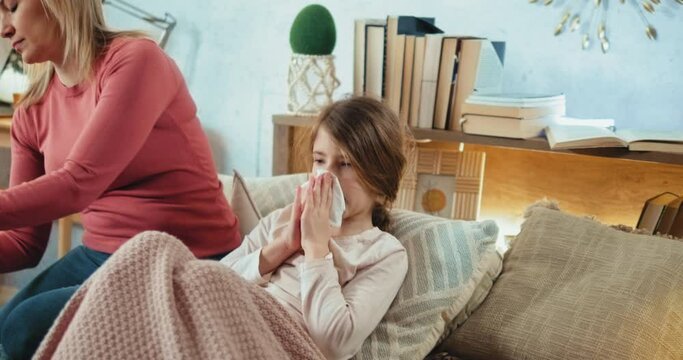 Mother gives ill sick child daughter medicine syrup at home. Sick little girl cleaning her nose
