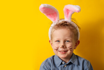 Cute boy with bunny ears smiling on yellow background copy space