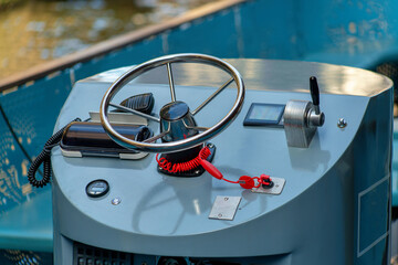 Boat steering wheel on metal plantform with different gears and levers to maneuver and direct ship in afternoon shade
