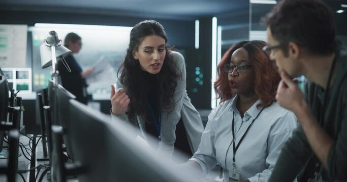 Team of Three Talented Young Software Engineers Use Computer to Discuss a Technological Project in Modern Industrial Office. Group of Male and Female Scientists Work in Research and Development Center