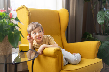A little boy sits in a chair and communicates with a smart speaker