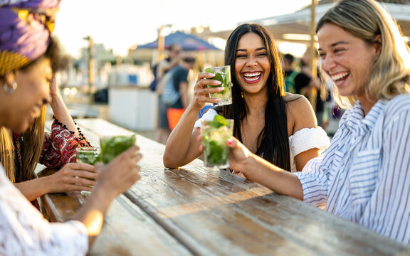 Young women celebrating at beach chiringuito, focus on brunette woman with toothy smile