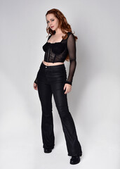 Full length portrait of beautiful woman with long red hair wearing black corset top and leather...