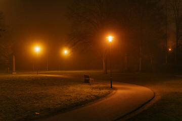 parkway in a foggy night with the orange illuminated street lamps