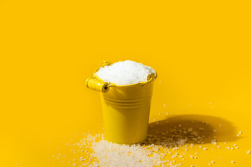 Coarse white salt in a yellow metal small bucket on the yellow background. Free space for text