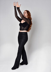 Full length portrait of beautiful woman with long red hair wearing black corset top and leather...