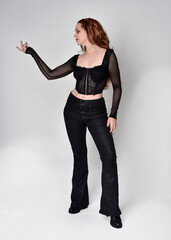 Full length portrait of beautiful woman with long red hair wearing black corset top and leather...