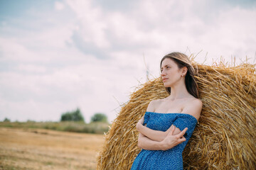 Portrait of a beautiful woman in a summer dress on a field among haystacks in summer.