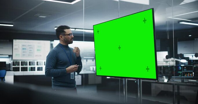 Multiethnic Lead Software Engineer Standing Alone in a Meeting Room, Using a Big TV Display with Green Screen Mock Up Template with Potential Information Created by Development Department
