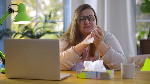 Woman at workplace works at laptop coughs and wipes her nose with napkin. Realtime