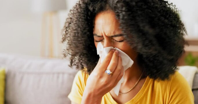 Sick, tissue and woman blowing her nose while sitting on a sofa in the living room of her house. African female sneezing while relaxing on a couch with a flu, cold or allergies in her modern home.