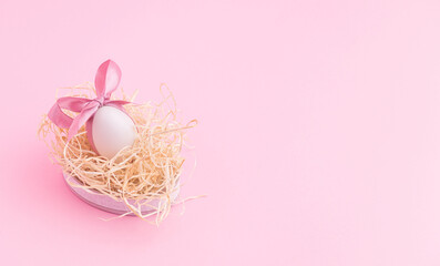 Wide pink Easter background - white egg with cute bow lying in a straw nest, sleeping egg