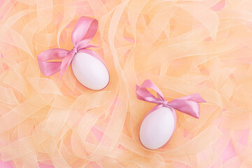 Two white eggs with cute pink bow lying on a heap of shiny ribbon