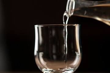 girl hands pouring red wine into a glass from a clay bottle on a black background