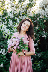 a beautiful woman in a pink dress stands with lilacs in her hands