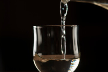 girl hands pouring red wine into a glass from a clay bottle on a black background