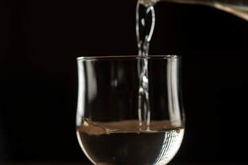 girl hands pouring red wine into a glass from a clay bottle on a black background