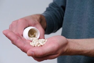 male hand spilling, stretches on palm white pills, capsule or vitamins on blurred light background, concept panacea for all diseases, placebo pill, overdose, people drug addiction problems