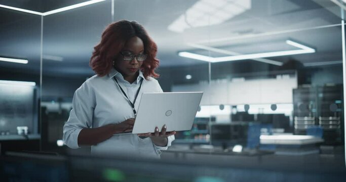 Portrait of a Technological Software Engineering Department Manager Standing and Using a Laptop Computer. African Female Looking in the Distance and Thinking while Working in the Office