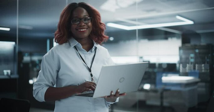 Portrait of a Black Diverse Female Wearing Glasses, Using Laptop Computer, Looking at Camera and Smiling. African Information Technology Specialist, Software Engineer or Developer