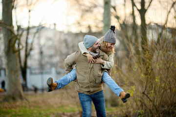 A handsome man giving his girlfriend a piggyback ride outdoors