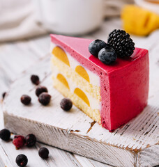 A slice of a pink strawberry cheesecake served with fresh berries on a white board