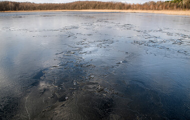 The texture of thin melting ice on a spring lake with the sky reflected on the surface. Light glare.