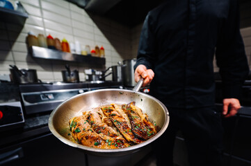man chef cooking fried meat slice in frying pan on restaurant kitchen